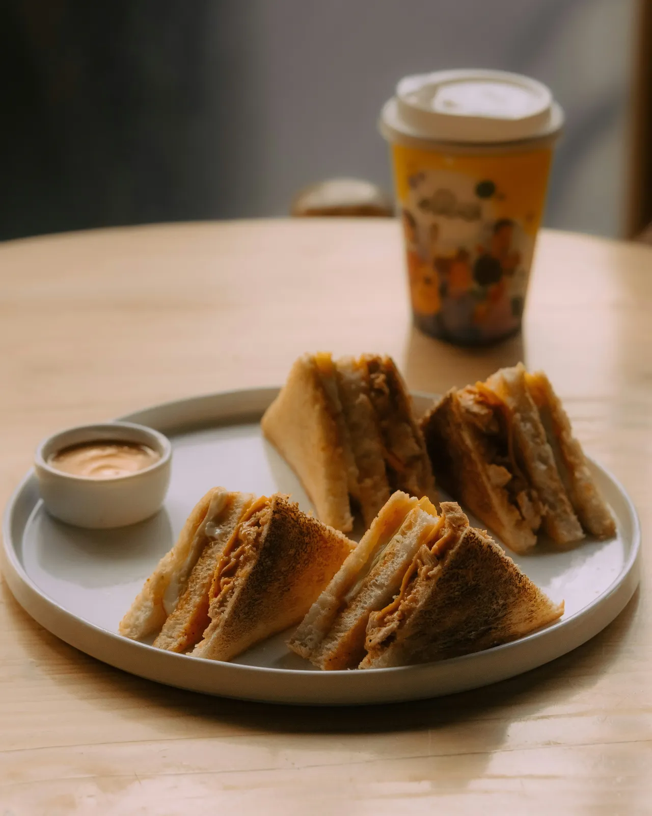 Toasted sandwich triangles on a plate with a dipping sauce and iced coffee